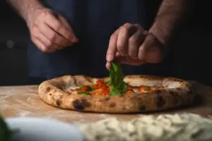 Person tilføjer frisk basilikum til pizza